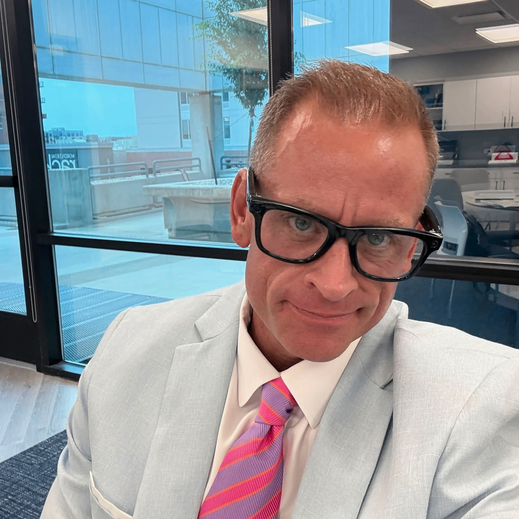 Portrait of Dr. Dave Haws, founder of Your God Body, wearing glasses and a light blue suit with a striped tie.